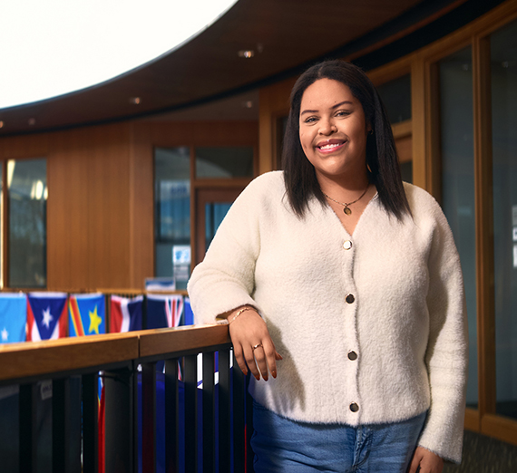 Una mujer está de pie con los brazos cruzados junto a una ventana.